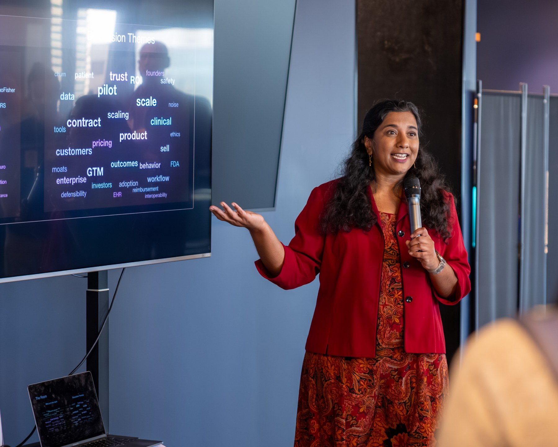 Arvita Tripati speaking to a healthtech audience beside a slide of session themes